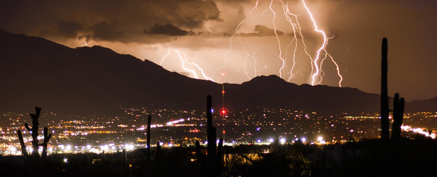 Photo of monsoon in Arizona. Series of lightning behind the mountain, rain cloud forming, overlooking the city lights and spiking saguaro trees.
