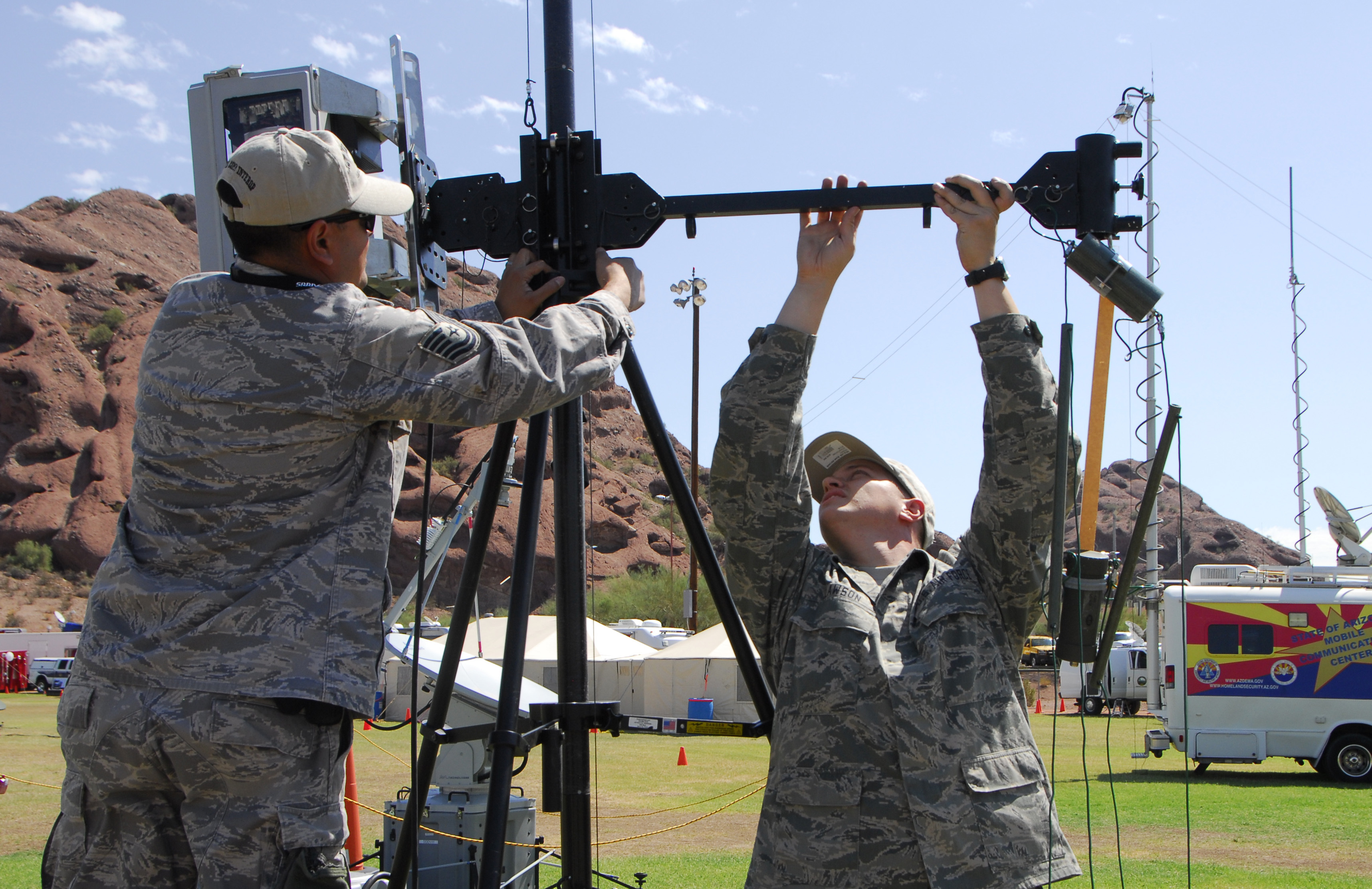 PAO. Military personnel set up cameras and radio equipment around the Papago Military Base. On a sunny day, you can see red mountains in the background.