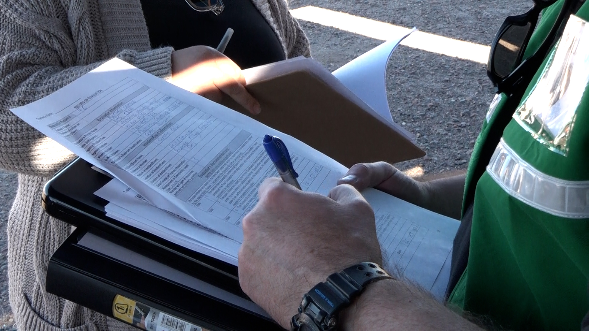A photo of an evaluator (wearing a green vest) signing off the AQS form while holding binders underneath the paper form.