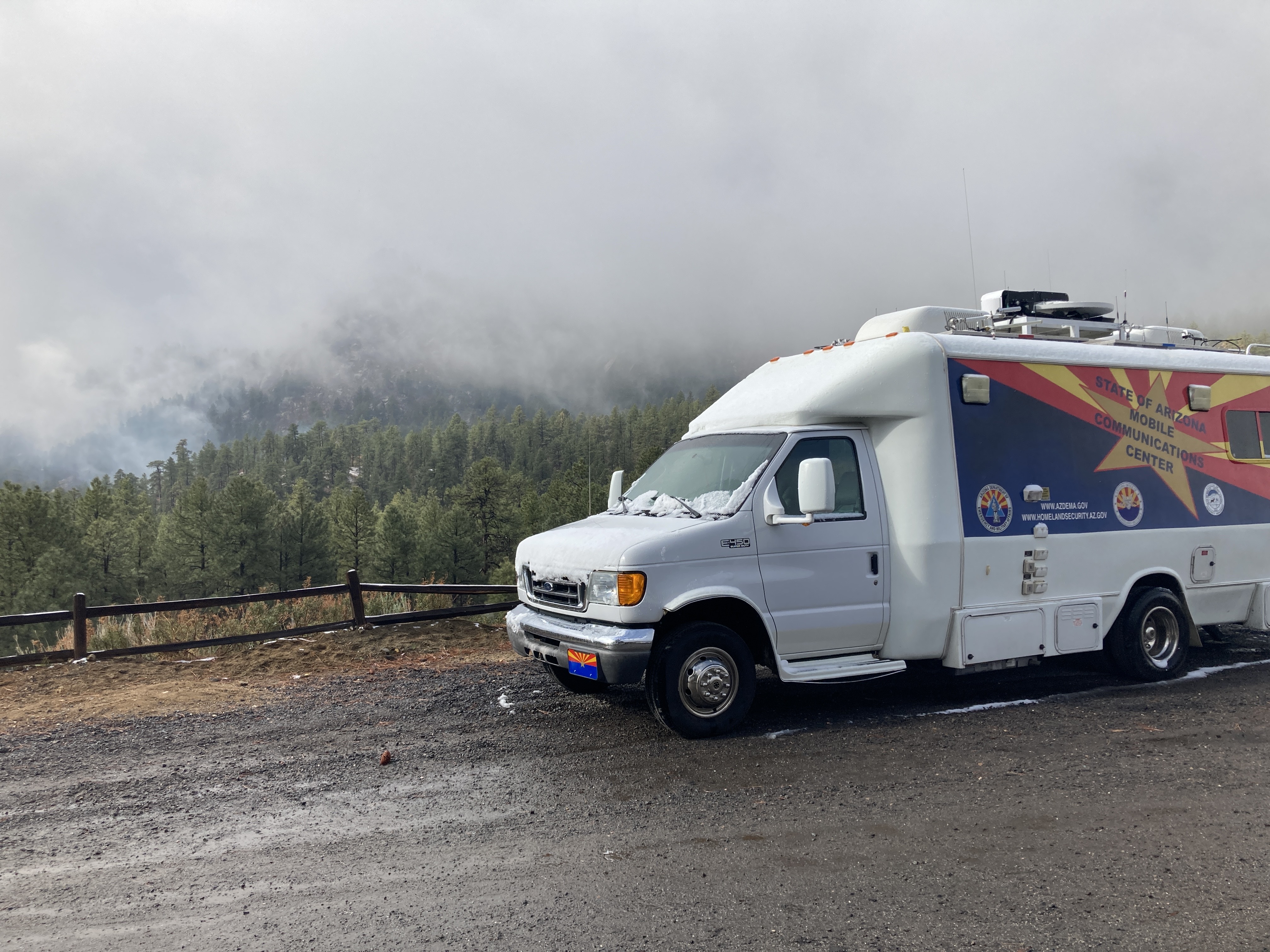 A photo of the "Toad" mobile communications center, parked on the side of the road, with snow covering part of the windshield and hood of the vehicle, with foggy mountain background.