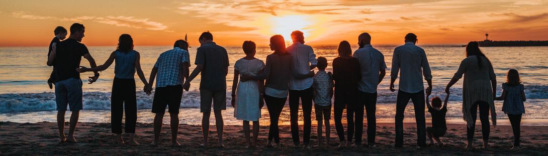 Service Member and Family Resources. Image of Fourteen family members lined up next to each other, holding hands and hugging each other as they stared into the horizon at sunset on a beach. Clouds above them, there are Illuminated by the glare of the Sun.