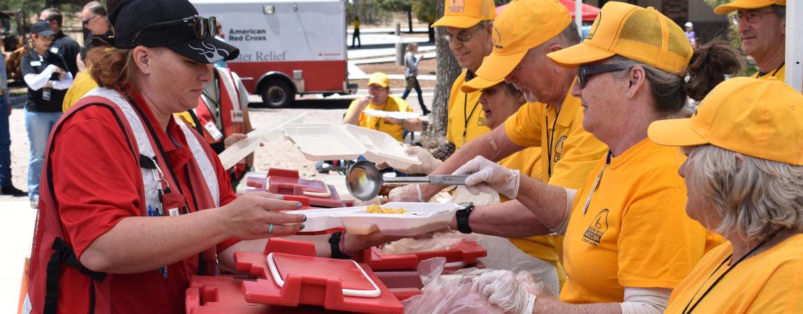 Photo of Disaster Relief Arizona volunteers wearing yellow orange shirts and hats, serving fellow volunteers (Red Cross), and citizens at the Individual Assistance Service Center (IASC).