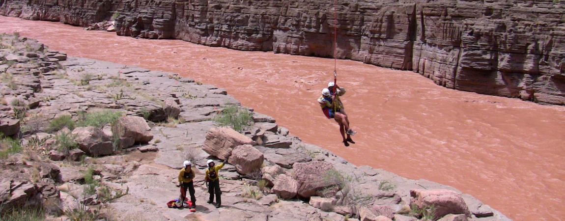 Photo of two people holding on to the line, and two rescue personnel on the ground. Search and rescue operation in the desert, caught on a flash flood.