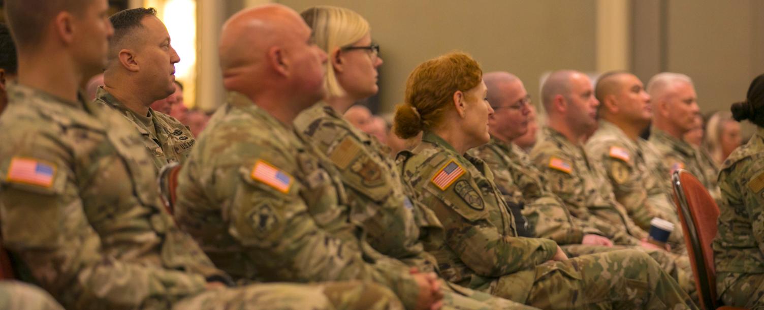 Military personnel sitting down in a ballroom atmosphere wearing Multicam.